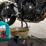 10W-40 motorcycle oil beside a motorcycle during PMS in a garage
