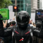 Amaron vs GS Battery featured image showing a helmeted rider in full gear holding both motorcycle batteries in a crowd