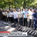 Confiscated open pipe mufflers Philippines enforcement scene in Valenzuela City showing officials inspecting seized motorcycle mufflers during a public ceremony.