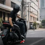 Nmax V3 Issues and Problems guide showing a scooter rider checking the rear brake during daily city riding