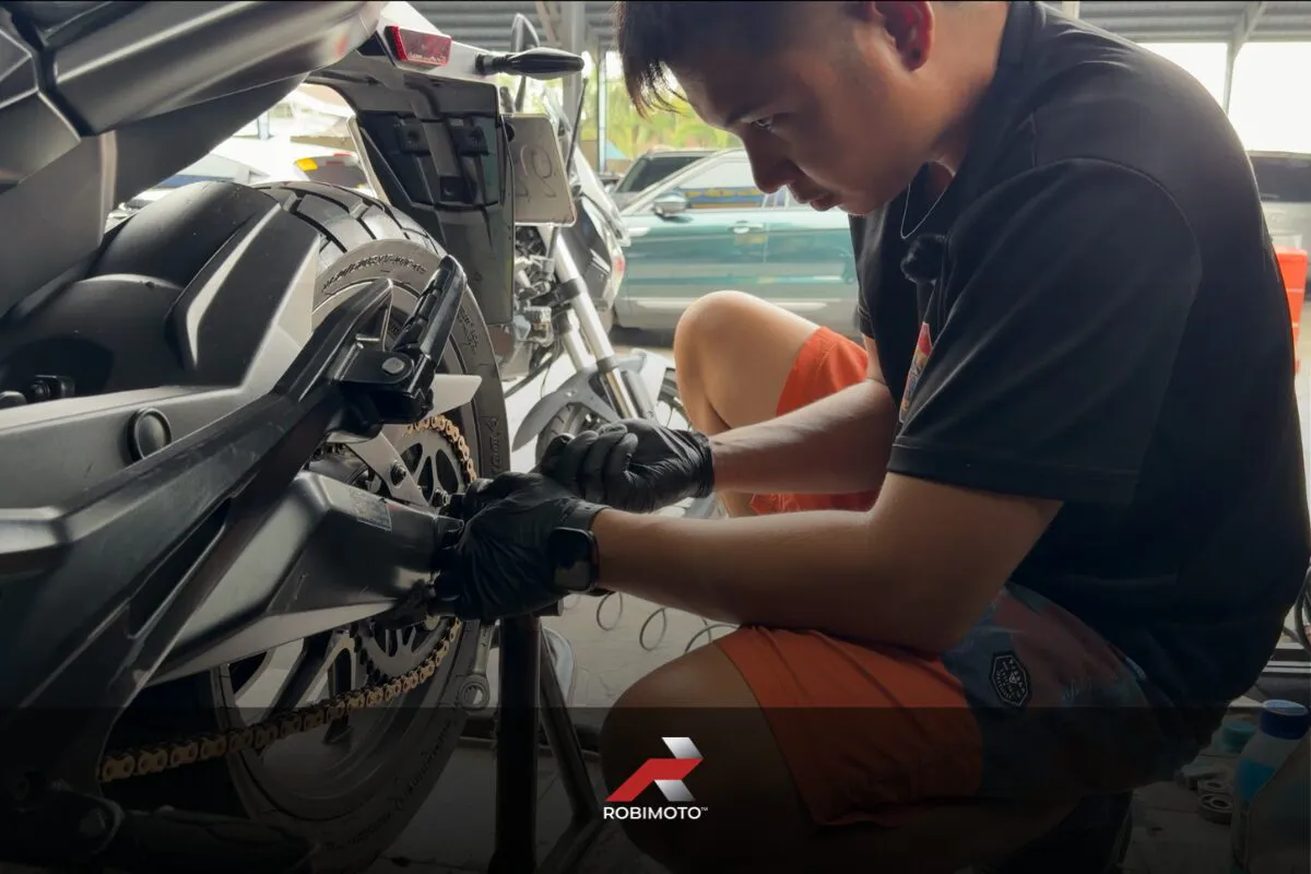 Motorcycle mechanic inspecting a chain drive for a motorcycle chain vs belt vs shaft drive comparison guide.