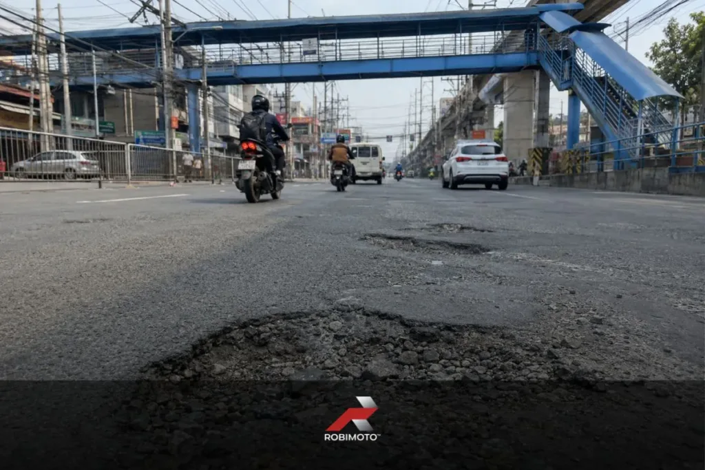 Low-angle featured image showing a large pothole on McArthur Highway in Valenzuela City, highlighting motorcycle road safety Philippines concerns